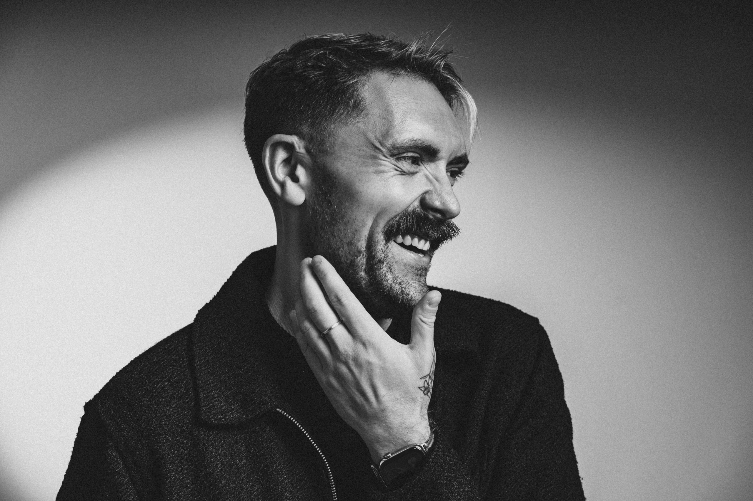 Jordon smiling in profile with his hand at his chin, in black and white.