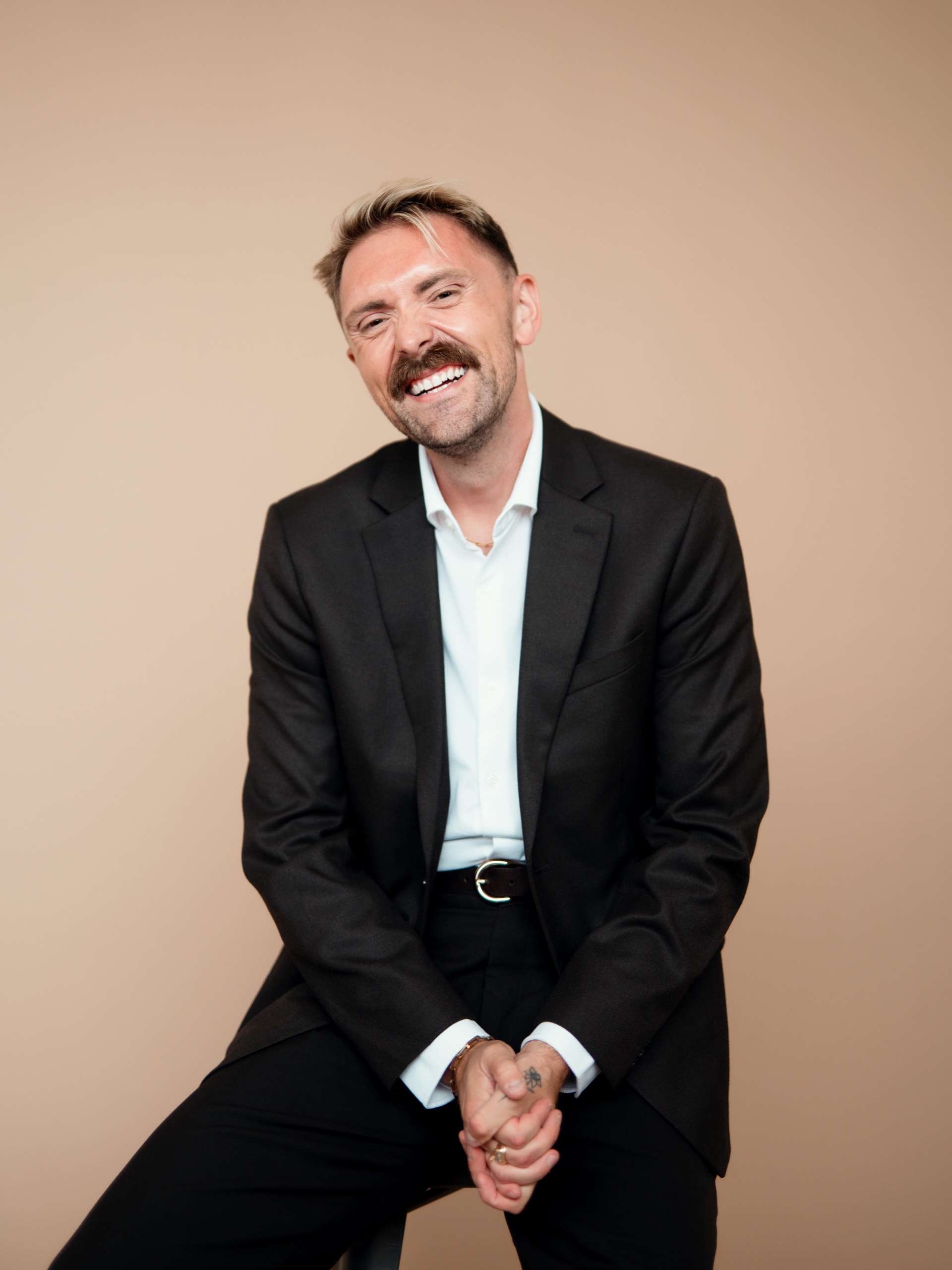 Jordon laughing while seated in a black suit.