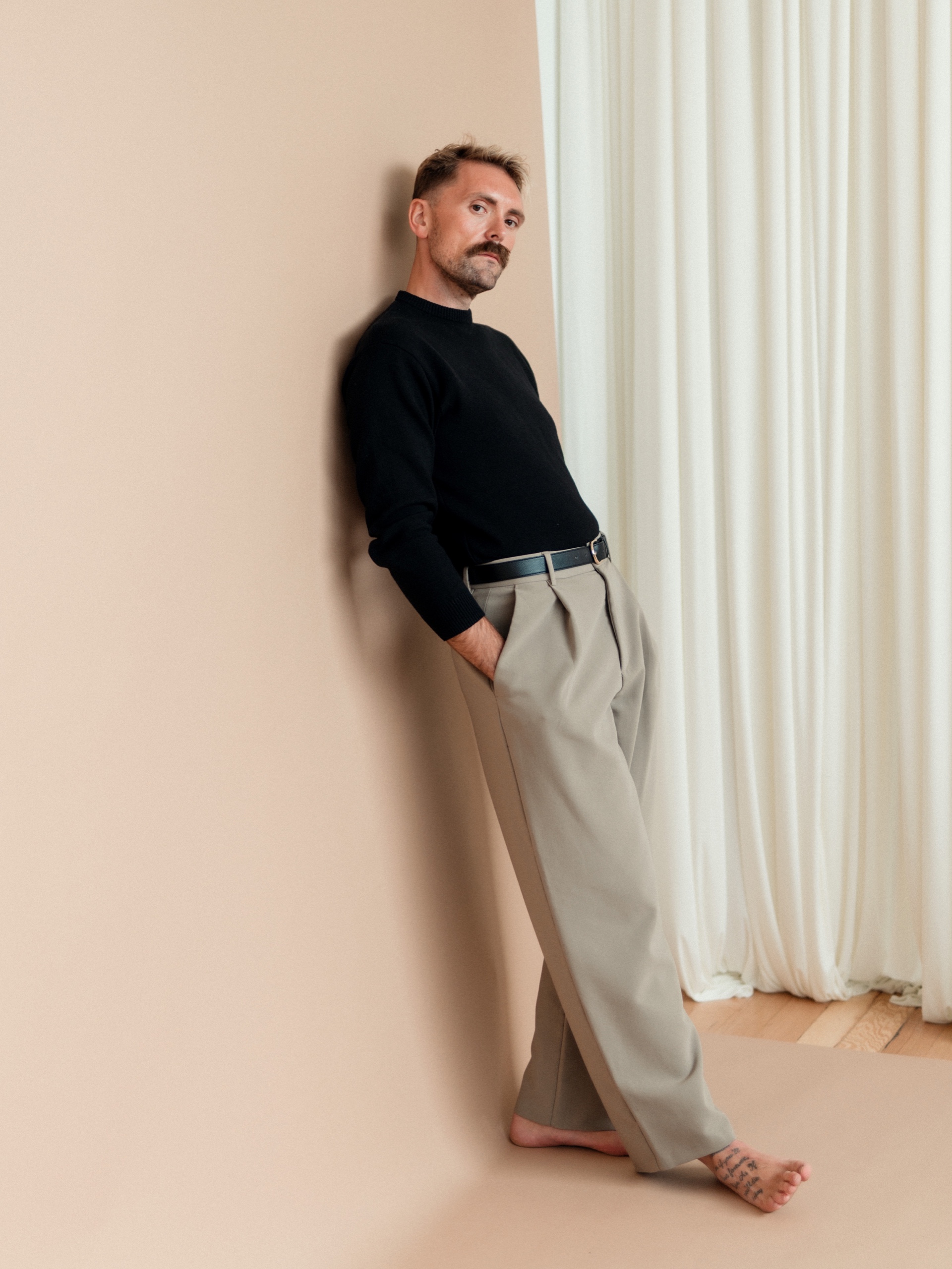 Jordon barefoot in a black sweater and tan trousers.