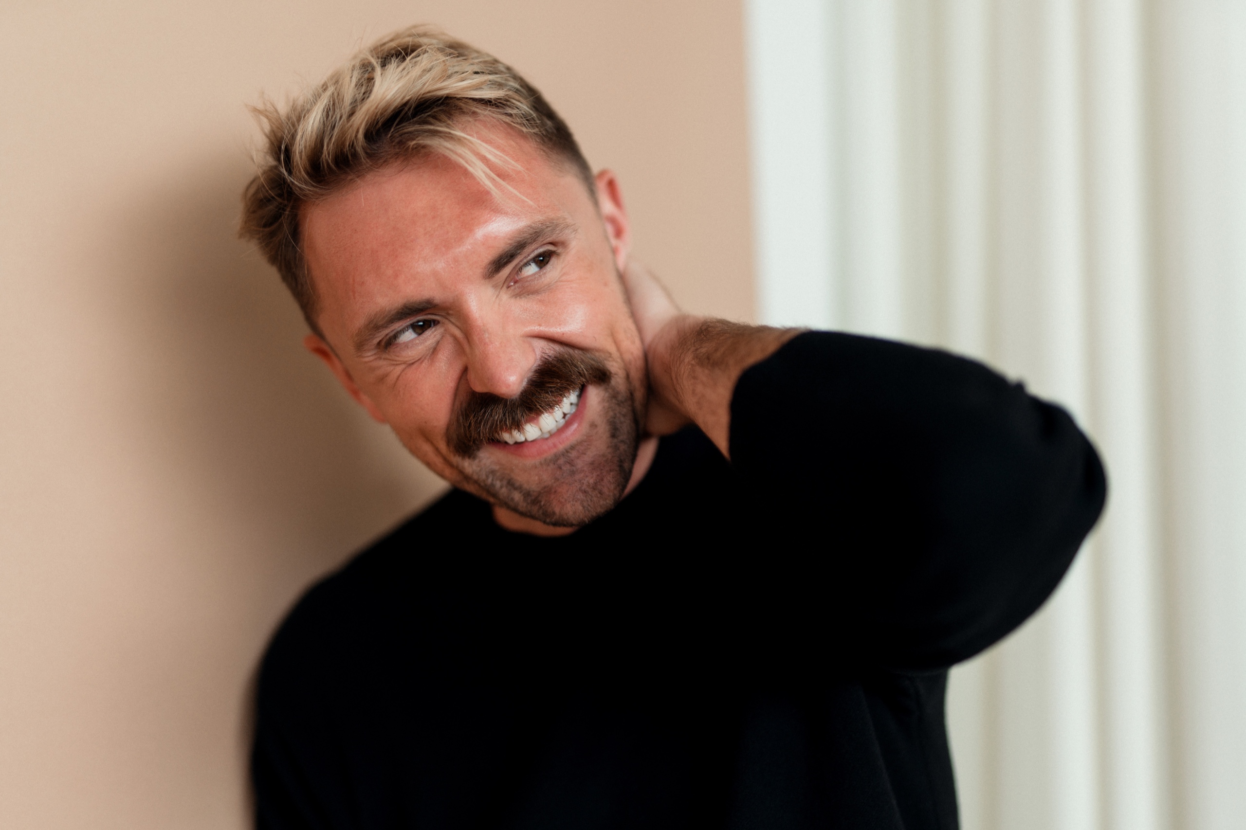 Close portrait of Jordon smiling with a hand behind his neck.