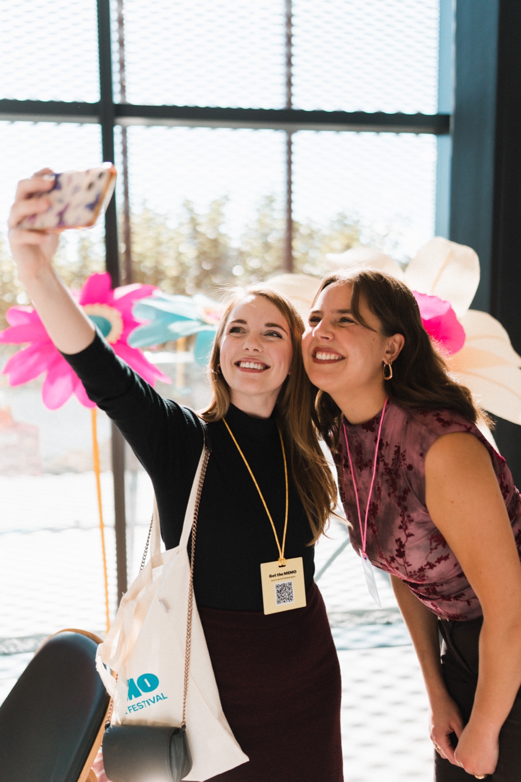 Two Memo Creative Festival attendees take a selfie beside colourful flower decorations.
